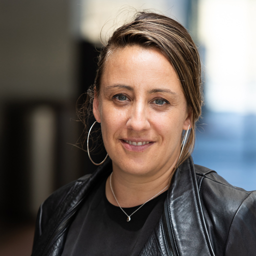 Cecile Puretz, Assistant Director, Disability Access and Inclusion is wearing a black leather jacket, silver earrings, and is smiling broadly at the camera.