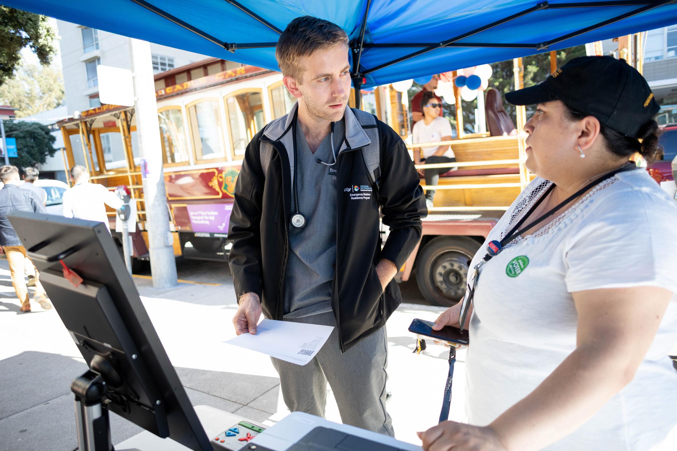 Jay Roever, MD, left, resident in Emergency Medicine, talks with Evangelina Pena Avila, a poll worker with the City & County of San Francisco Department of Elections