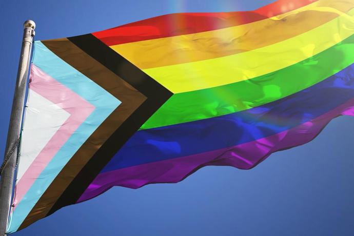 Inclusive LGBTQIA+ flag designed by Daniel Quasar waving from a flag pole