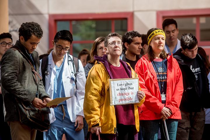 UCSF community members gather at an outdoor day-time protest. A person in focus is holding a sign that reads,'Love gives us hope that change is  possible'.