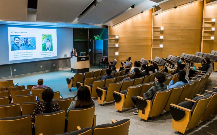 Julieta Lamm-Perez, a CURE intern, presents their research presentation in front of a crowd inside UCSF's Byers Auditorium at Mission Bay.