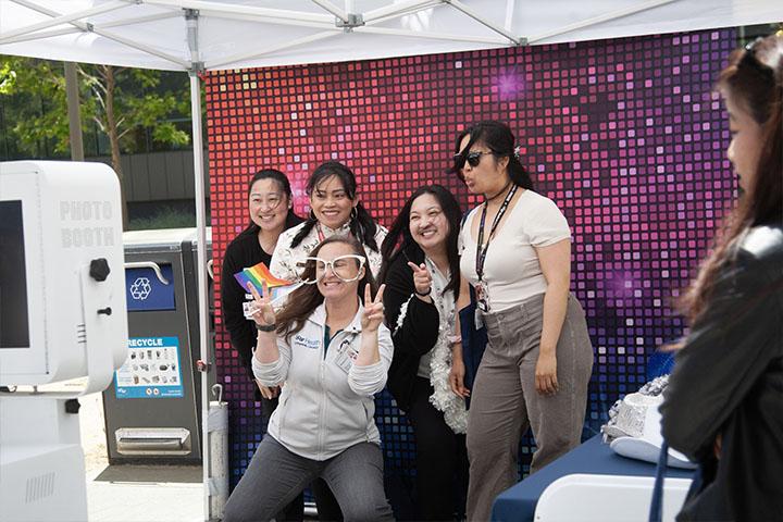 Five UCSF community members posing in front of an automated photography stand, some wearing oversized glasses, making humorous facial expressions and hand gestures.